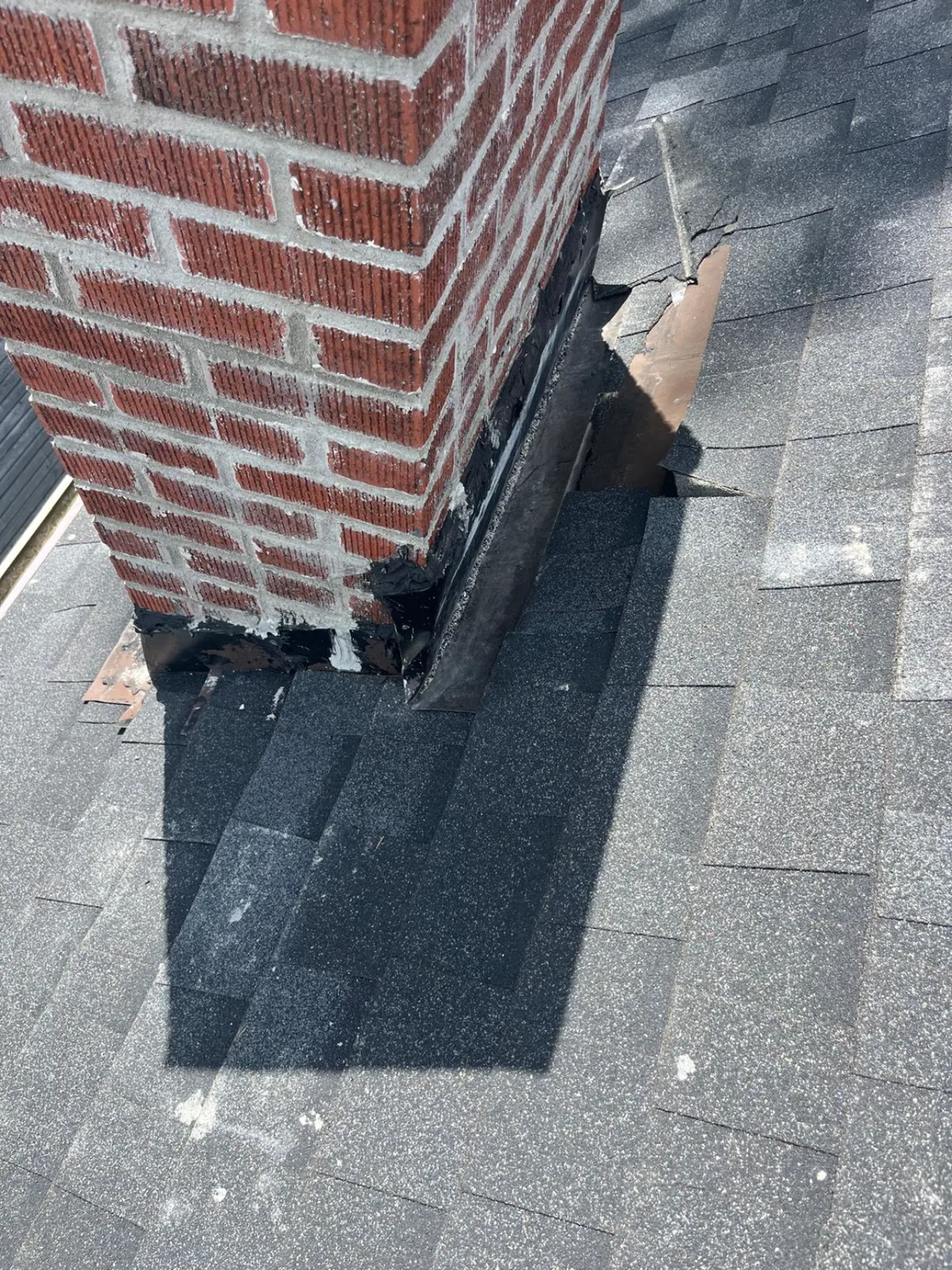 Failed chimney flashing on a Pittsburgh roof with roofing tar smeared over the joint by a previous repair